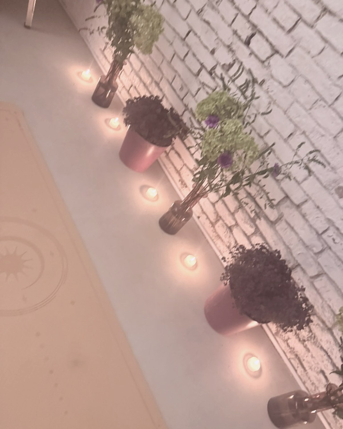 Candles and plants lining the floor along the brick wall